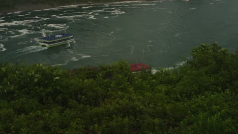 Two iconic tour boats, one red and one blue, cruise through the swirling waters of Niagara River toward the misty base of Niagara Falls