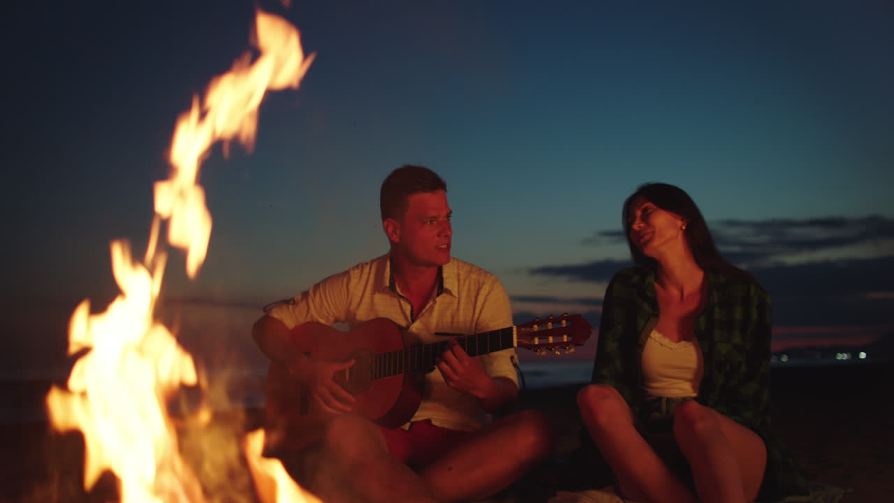 해가 지는 해변에서 캠프불 에서 기타를 연주하는 부부