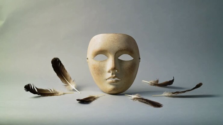 Luce chiave brillante che fa muovere la piuma sinistra accanto a una maschera facciale su un tavolo da studio, con un riflesso che si sposta