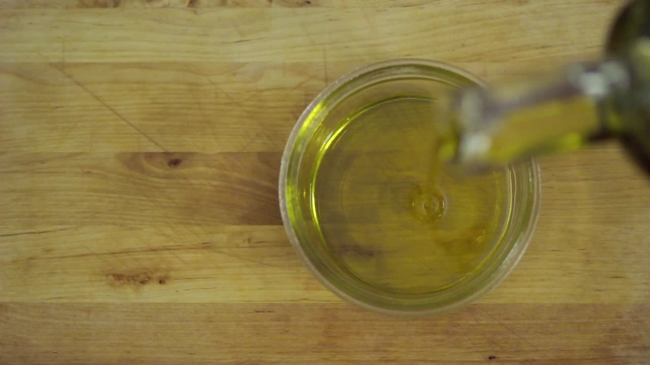 Versare olio d'oliva in una ciotola di vetro su una tavola di legno