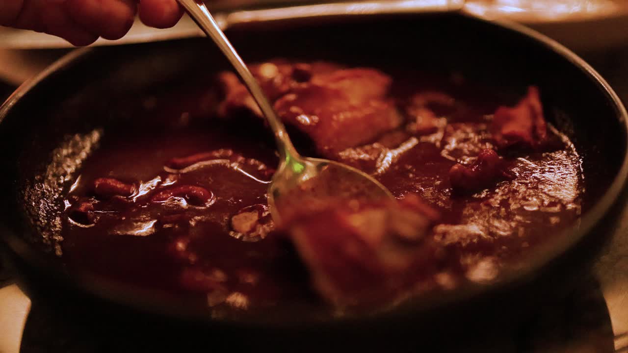 A simmering stew is stirred in a dimly lit kitchen, creating a warm and inviting atmosphere