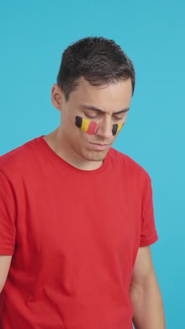 man with belgian flag painted looking away with serious expression