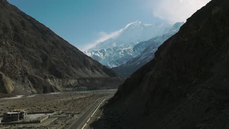 drone subiendo sobre la carretera más allá de la sombra del valle para revelar las montañas cubiertas de nieve del valle de hunza