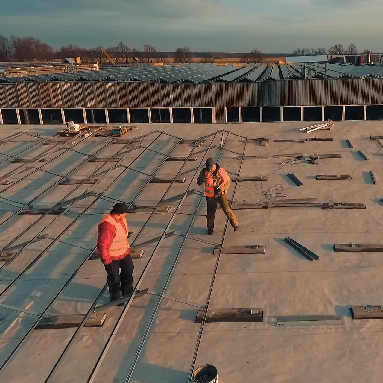 Installation of solar panels on a rooftop. Two workers in uniform install metal basis for sunny batteries at sunset. Aerial view.