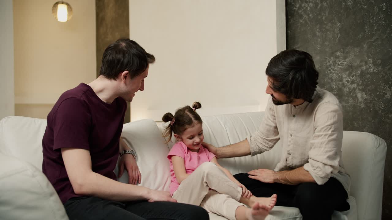 동성애자 부부 또는 삼촌이 소파에서 작은 소녀와 이야기하고 앉아 있습니다.