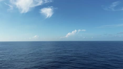 panning right extreme wide shot of a beautiful empty caribbean ocean landscape with no land or anything in site and calm blue water below on a warm sunny summer day with a few clouds