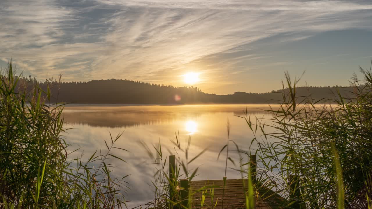 un lapso de tiempo del amanecer, reflejado en la superficie quieta del lago, se eleva sobre el bosque oscuro