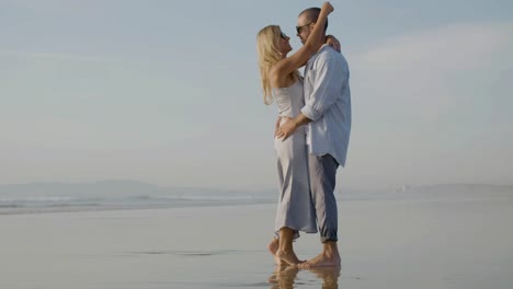 Happy-Caucasian-couple-in-sunglasses-dancing-at-sunset-on-beach.