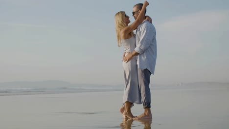 una feliz pareja caucásica con gafas de sol bailando al atardecer en la playa.