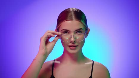 blonde caucasian woman looks at camera and adjusts her reading glasses with a friendly attitude, close-up shot of torso in studio