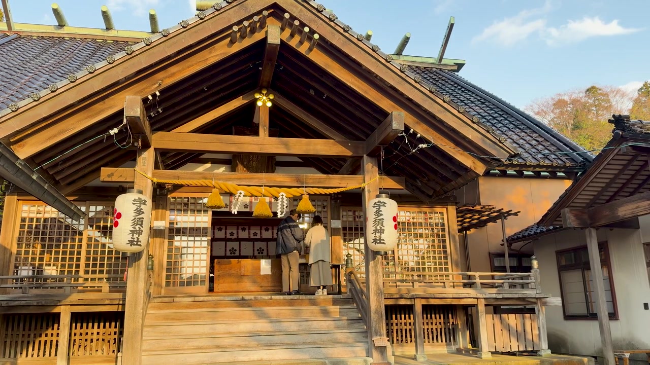 A couple prays at the entrance of Utasu Shrine under warm golden hour sunlight