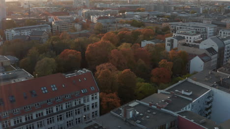 Vuelo-Por-La-Tarde-Sobre-El-Barrio-Urbano.-árboles-De-Colores-Otoñales-En-El-Parque-O-Cementerio-Entre-Varios-Edificios.-Berlín,-Alemania.