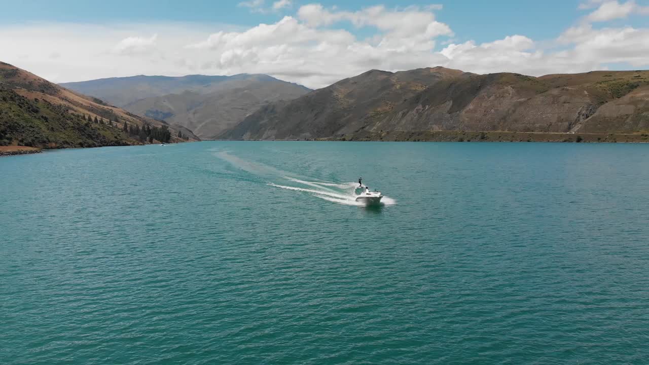 클라이드 댐, 중앙 오타고, 산과 구름이 배경에 있는 뉴질랜드 근처 던스탄 호수에서 보트 뒤에서 수상 스키
