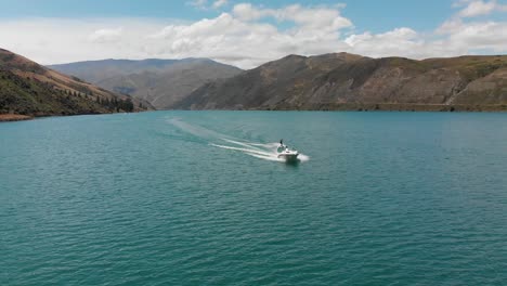 esquí acuático detrás de un barco en el lago dunstan cerca de la represa clyde, otago central, nueva zelanda con montañas y nubes en el fondo