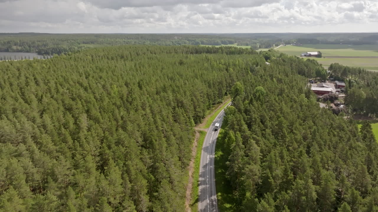 Aerial view approaching a RV driving on a paved, forest road, summer in Finland