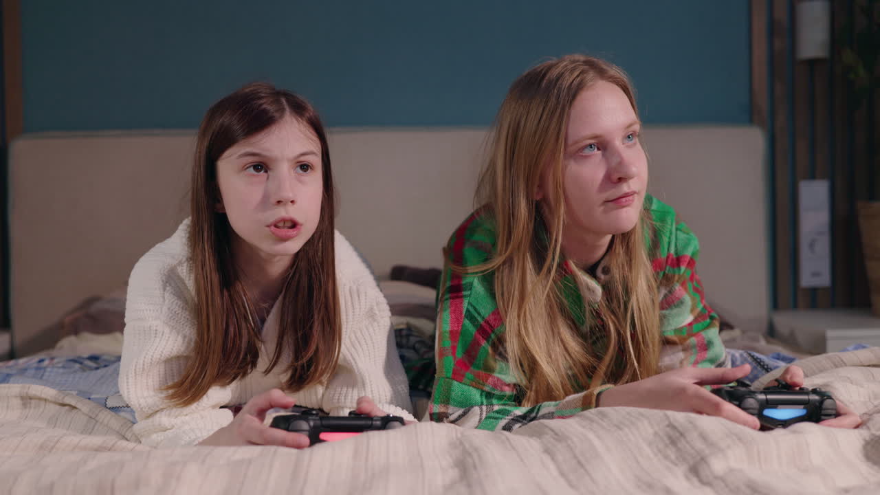Teenage girls playing video games on a bed