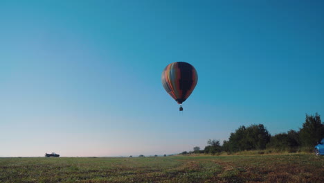 A-hot-air-balloon-taking-off-from-a-flat-field,-against-the-backdrop-of-a-snowy-cloudless-sky