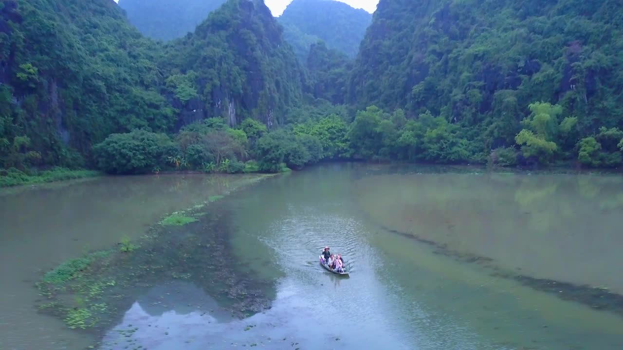 Cinematic drone footage of majestic limestone peaks in misty and foggy weather. Ricefields in wild jungle in the spring with boat tour canal in Tam Coc, Ninh Binh, Vietnam