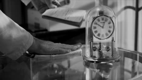 Comerciante-Retro-Vintage-Con-Bata:-Limpiando-El-Mostrador,-Reloj-Antiguo,-1950