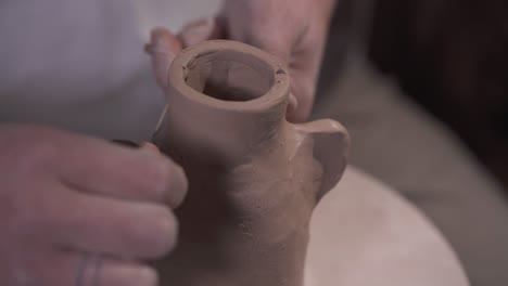 male hands are making handles of a clay jug cutting clay with a thread and fingers
