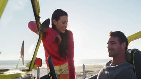 Happy-caucasian-woman-standing-next-to-man-sitting-in-beach-buggy-by-the-sea