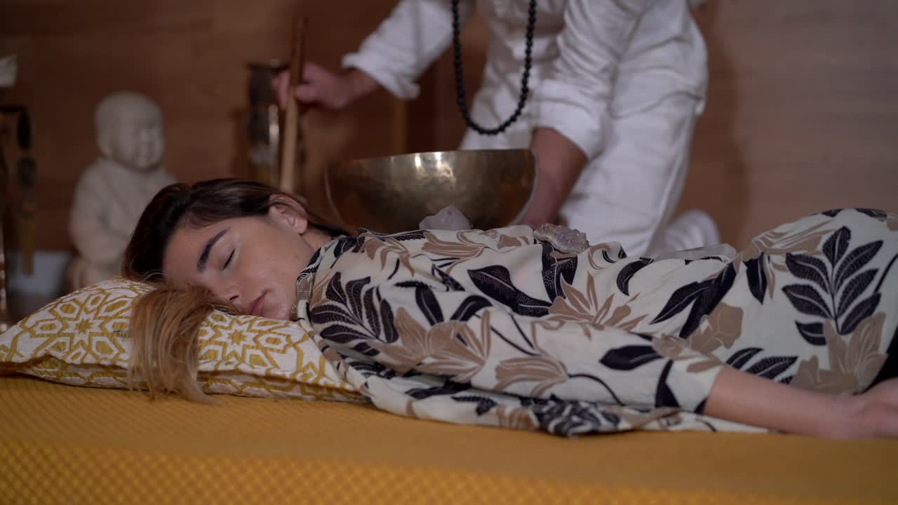 maestro zen tocando gong de tazón por encima de una mujer relajada durante la meditación