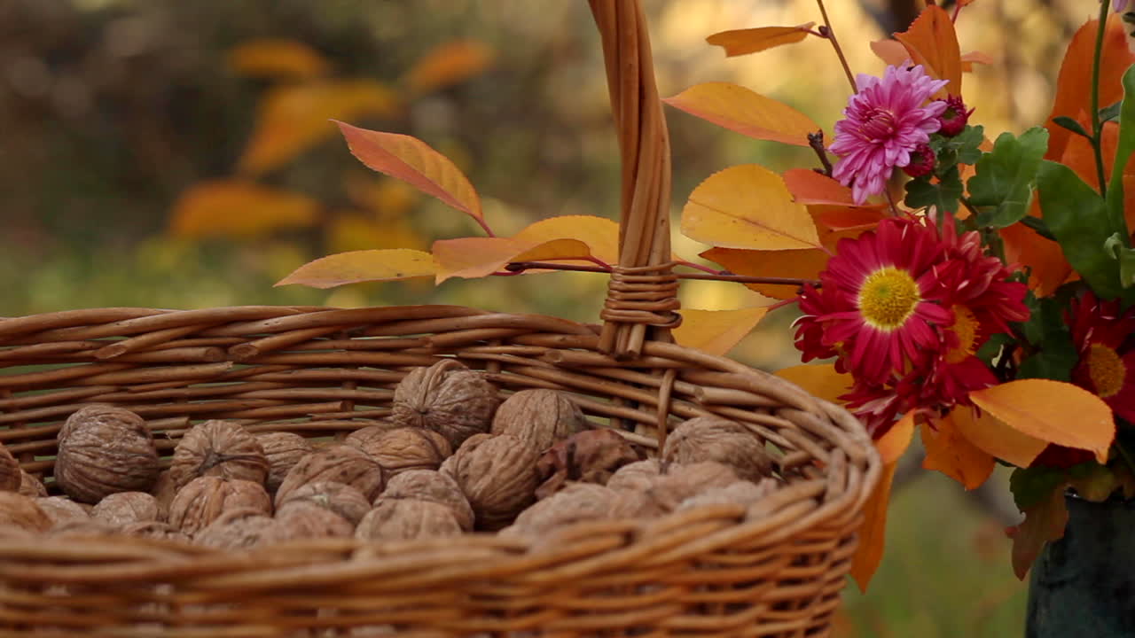 Cesto di vimini con noci accanto a un vaso di fiori all'aperto su un tavolo