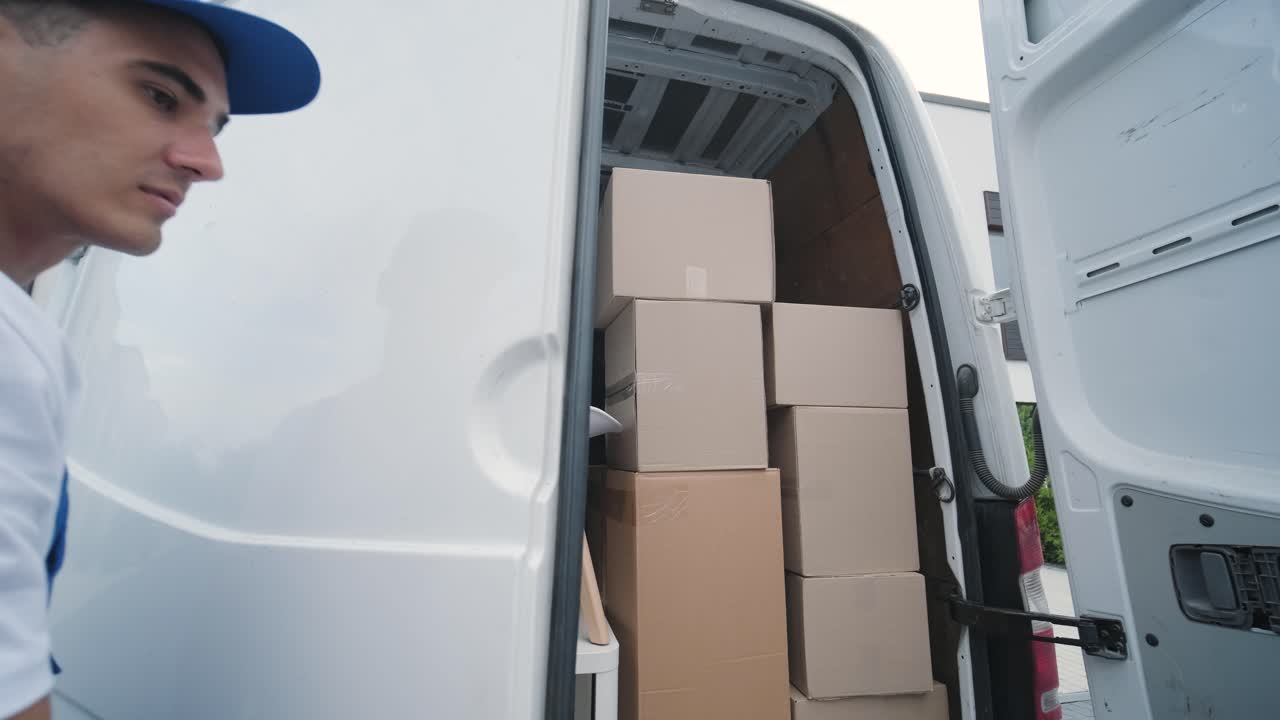 dos jóvenes trabajadores de una empresa de mudanzas descargan cajas y muebles del minibús en la casa del cliente