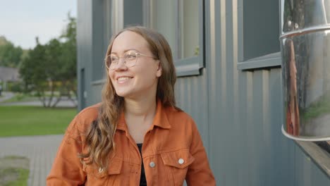 Strahlende-Brünette-Mit-Brille-Und-Orangefarbener-Jacke-Lächelt-Im-Urbanen-Ambiente