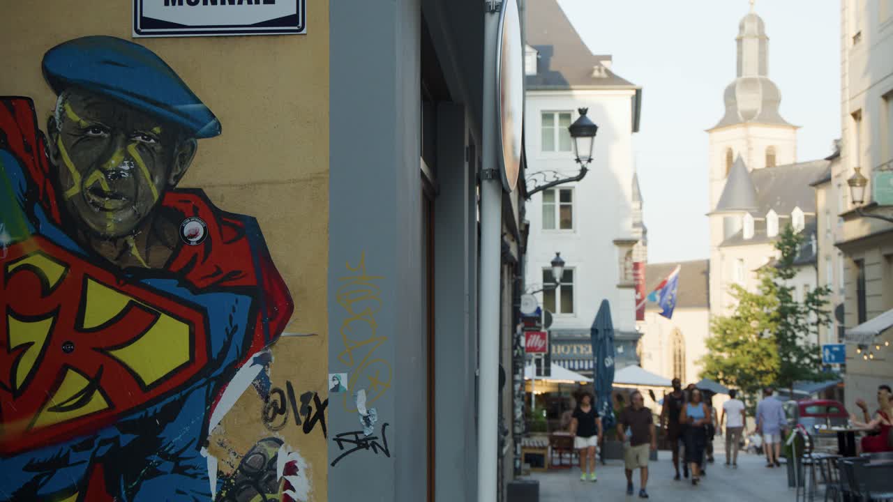 People stroll along a lively shopping street with outdoor dining, vibrant mural, and soft daylight