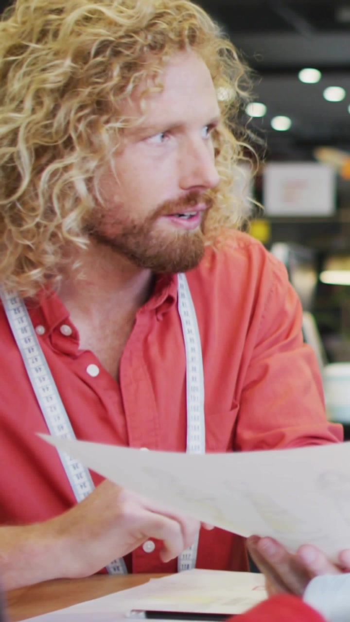 Male fashion designer tapping laptop causing metrics floating over papers while adjusting designs