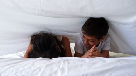 Happy-siblings-having-fun-under-the-bed-sheet-in-bedroom