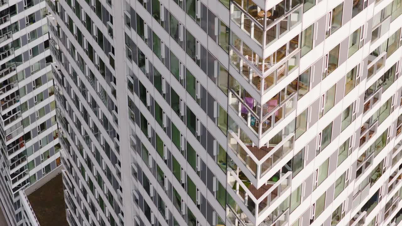 Close-up aerial view of intersecting residential skyscrapers with floor-to-ceiling windows and balconies, showcasing geometric patterns and contemporary urban living
