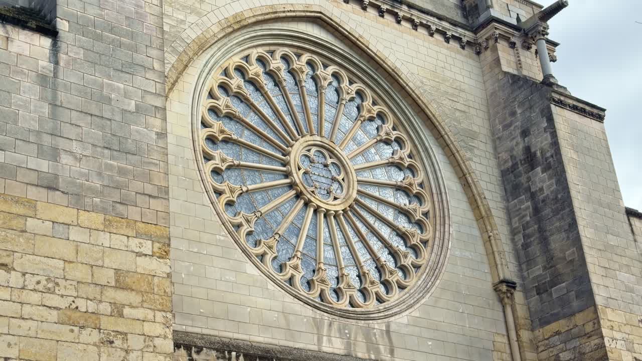 Rosettenfenster der Kathedrale Saint Maurice d’Angers mit radialem Steinmaßwerk, zentralem Okulus und spitzem gotischem Bogen, in die Kalksteinfassade unter sanftem Tageslicht gemeißelt, langsame Schwenk-Nahaufnahme.