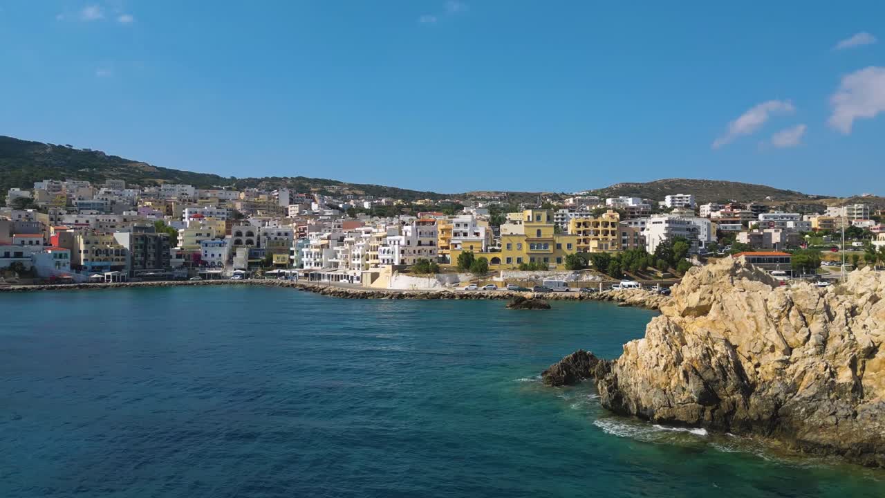 Foto aerea del lungomare del porto di Pigadia a Karpathos, Grecia, in una giornata di sole con cielo sereno, che cattura il porto, la costa e l'autentica atmosfera dell'isola