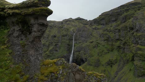 Filmischer-Flug,-Der-Einen-Riesigen-Wasserfall-Enthüllt,-Der-Durch-Eine-Klippenwand-In-Einen-Großen-Fluss-Und-Eine-Mit-Grünem-Moos-Bedeckte-Schlucht-Hinunterfließt