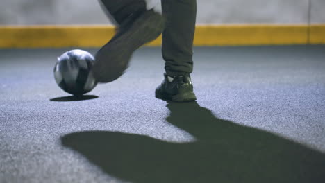 lower angle view of leg kicking soccer ball against wall under bright stadium lighting at night, showcasing athletic motion, shadows, and urban background