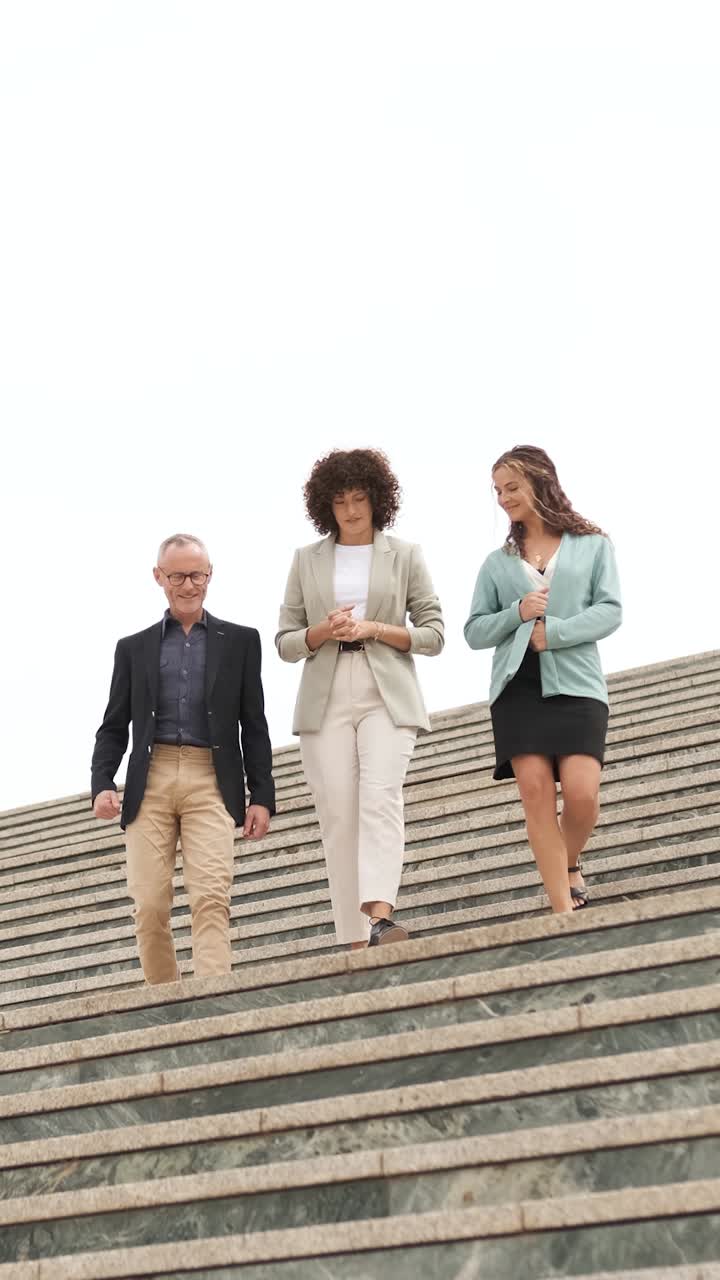 Diverse professionals discussing work while walking downstairs outdoors. Vertical