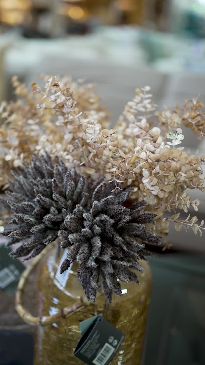 A collection of dried flowers showcases various textures and colors, elegantly arranged in a modern vase on a table, enhancing the room's warm atmosphere
