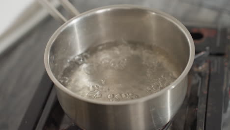 close up of water steaming and boiling vigorously in stainless steel pot placed on gas burner in kitchen, bubbles rapidly rising to surface, intense heating process visible