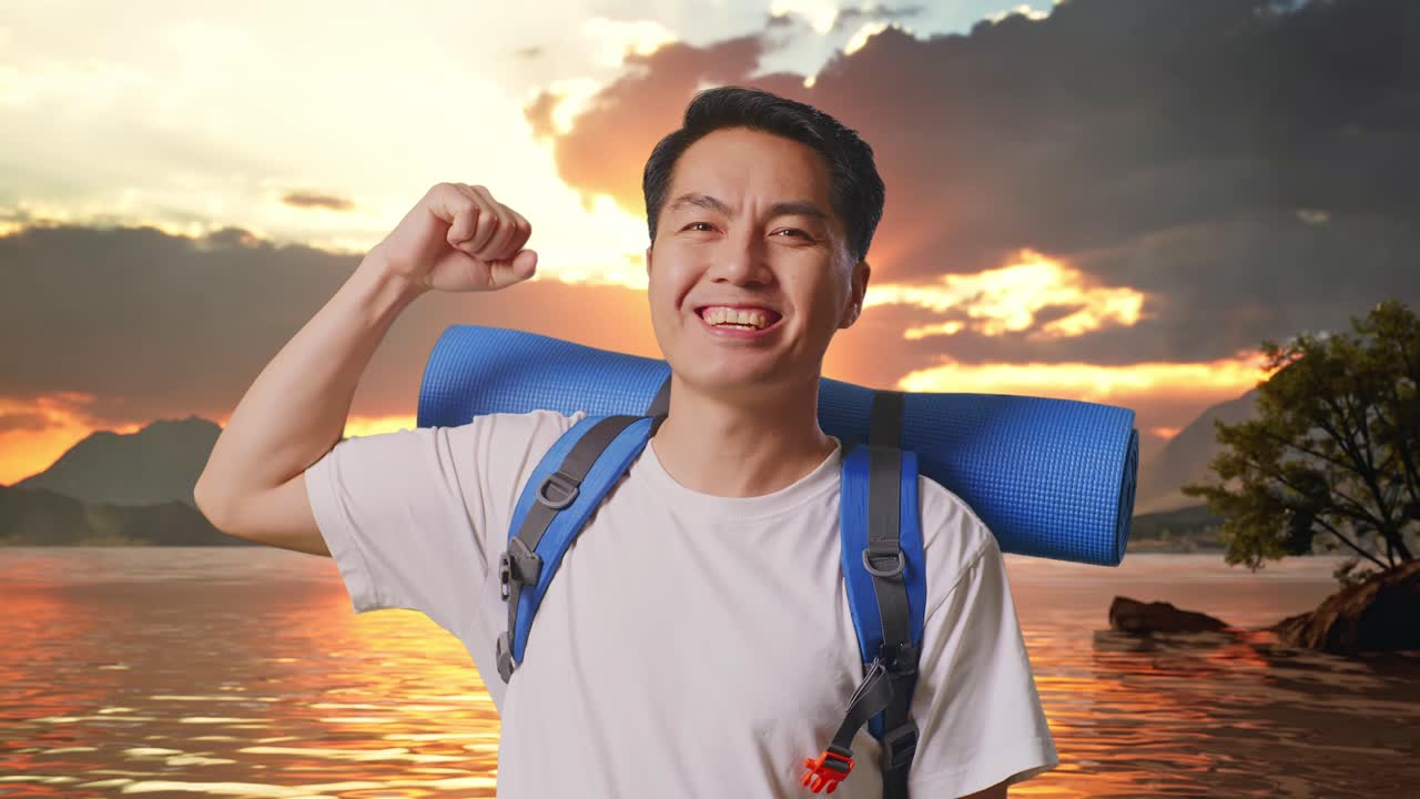 Close Up Of Asian Male Hiker With Mountaineering Backpack Smiling And Flexing His Bicep At A Lake