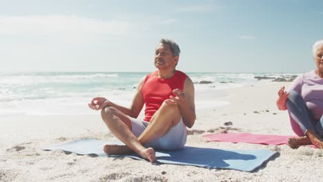 relaxed hispanic senior couple practicing yoga on mats on beach