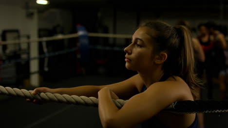 young woman leaning on a boxing ring rope in a gym