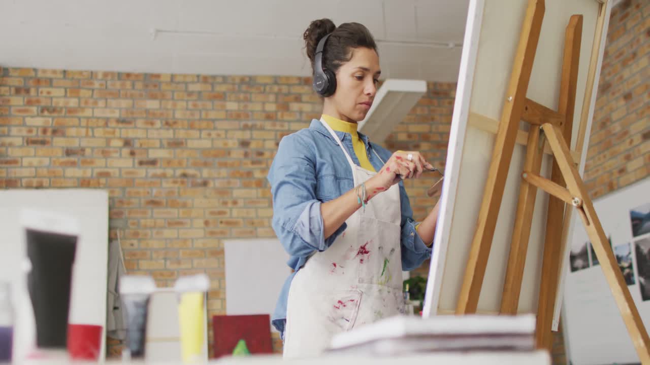 Video di un'artista donna birazziale con le cuffie che dipinge in studio
