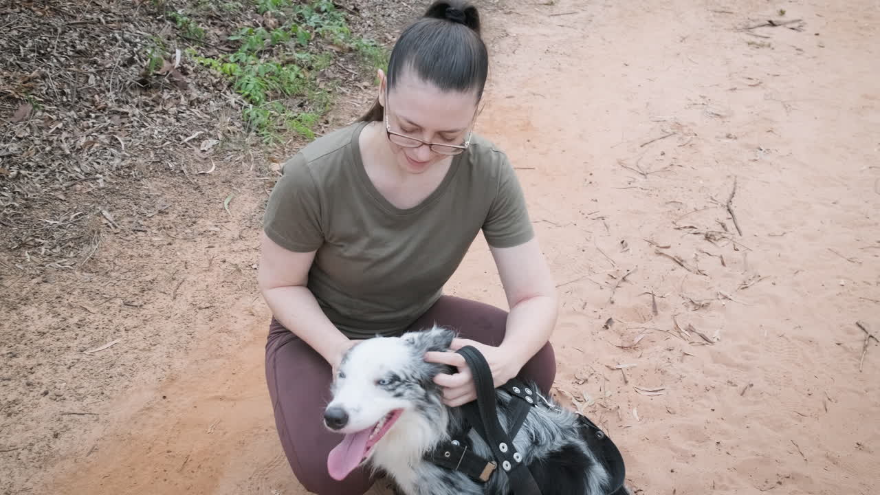 Woman with glasses having a nice time with her pet Australian Shepherd dog, petting him and playing with him in the forest
