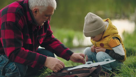 old fisherman is showing his fishing gear to little grandson happy family joint time in nature