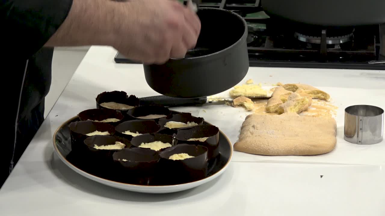A chef demonstrates the process of preparing chocolate cups filled with cream, showcasing techniques in a well-equipped kitchen during a culinary class. The setting is vibrant and engaging.