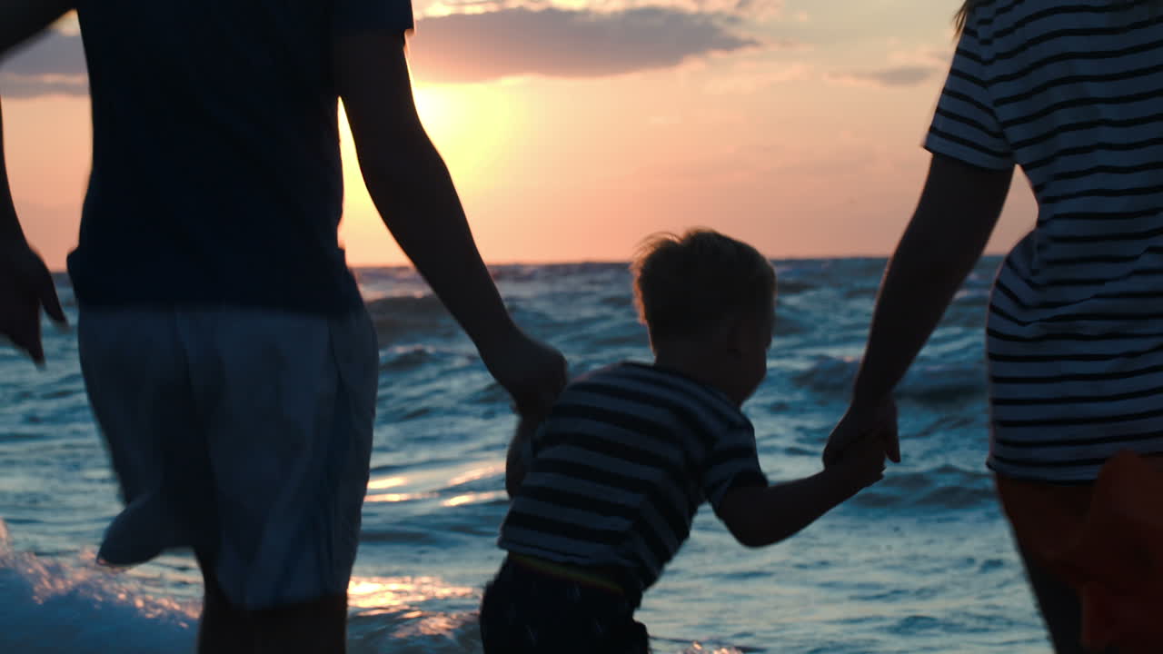 Glad familie på tre danser ved havet ved solnedgang