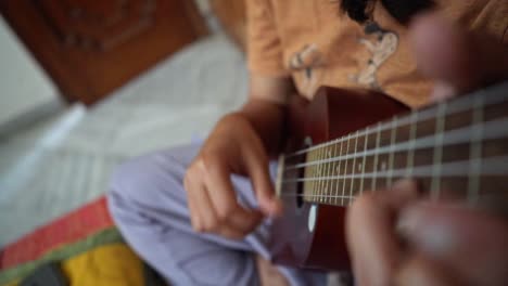 unrecognized person learning how to strum a ukulele at home