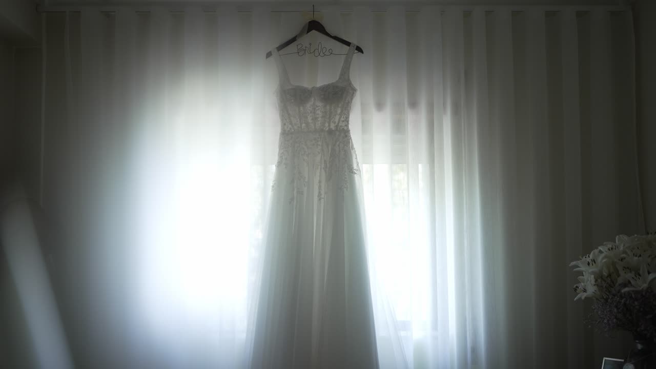 Wedding dress on a hanger against soft backlight from curtains in an elegant setting